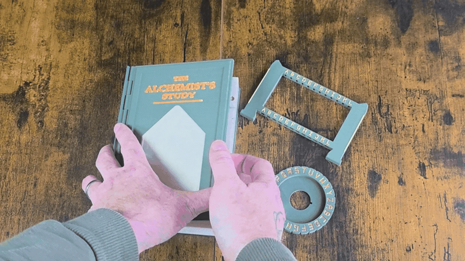 Jon’s real green Alchemist game-book prototype beside its frame and ring.