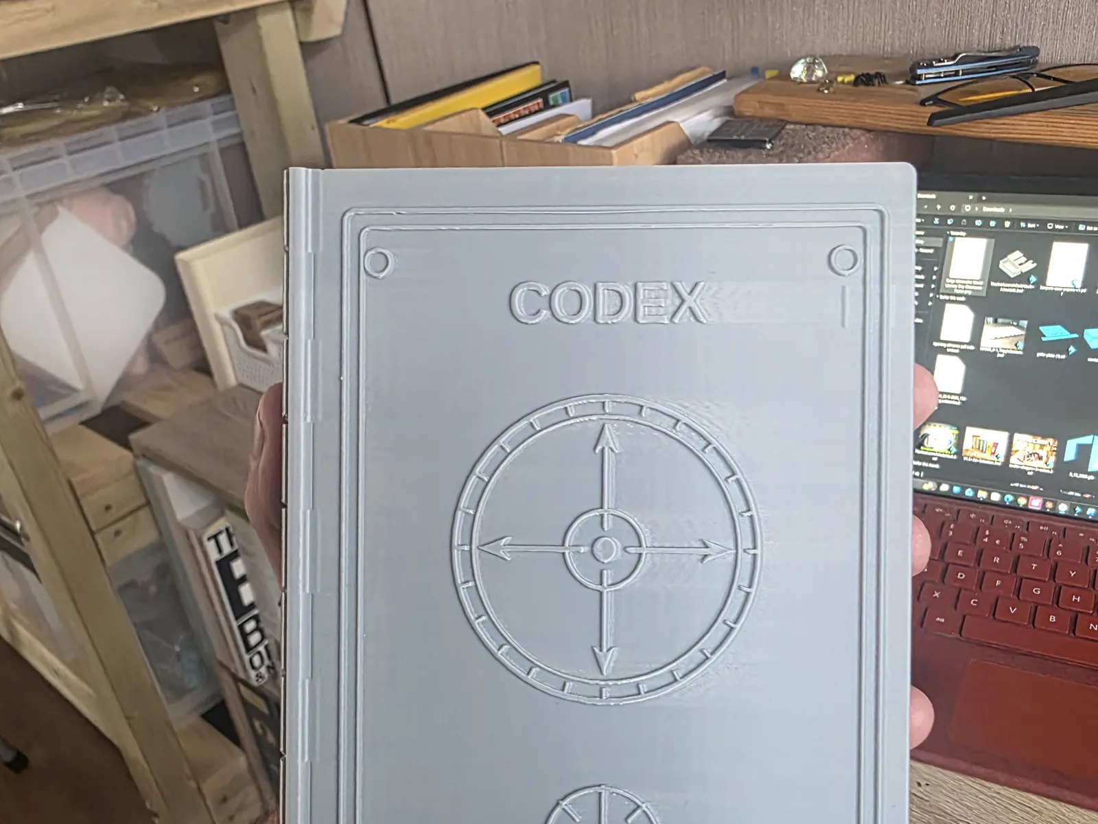 Front of an early grey 3D-printed Codex case held beside a workshop computer.