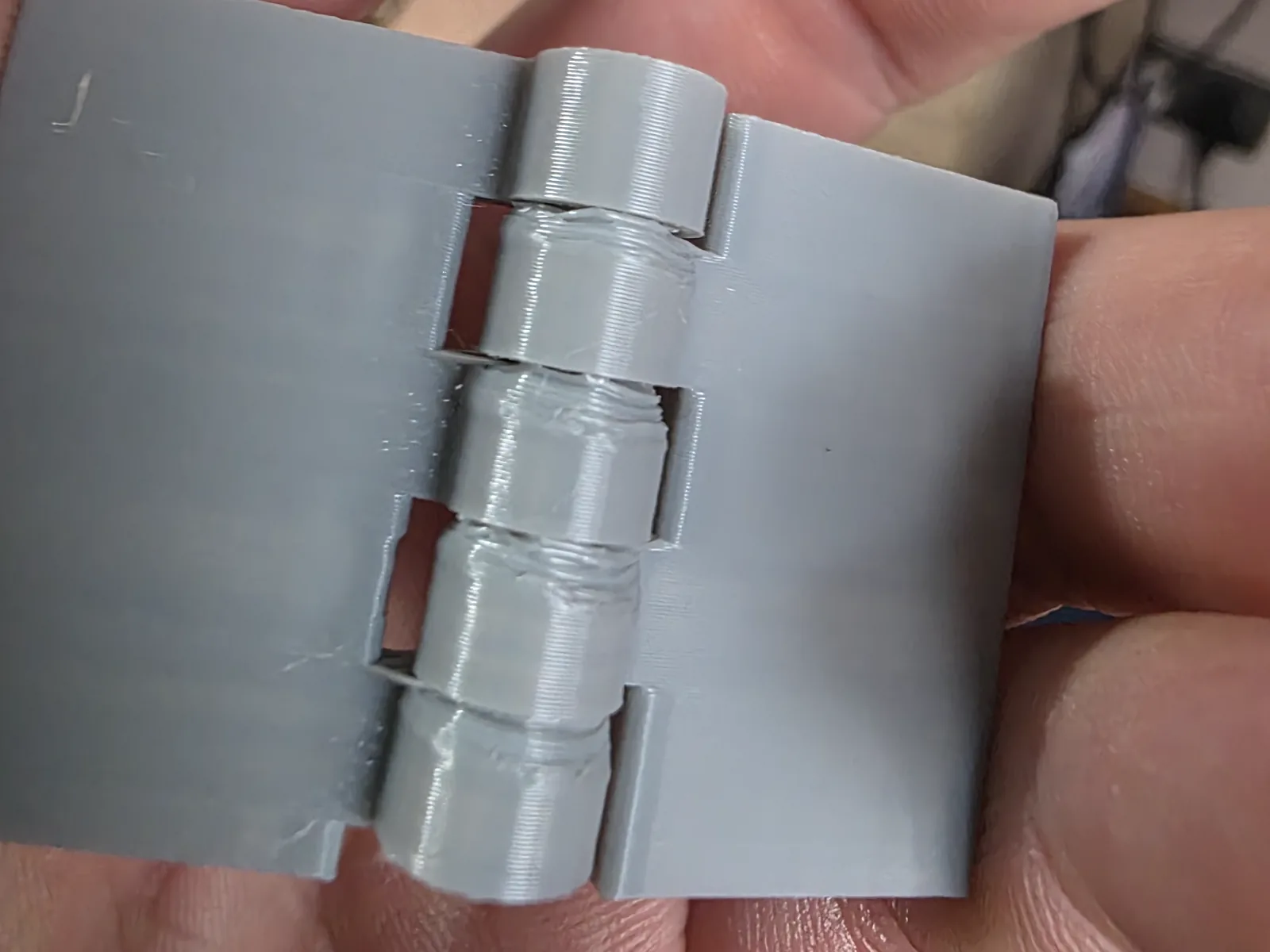 Close view of an early grey 3D-printed hinge with rough, misaligned joints.