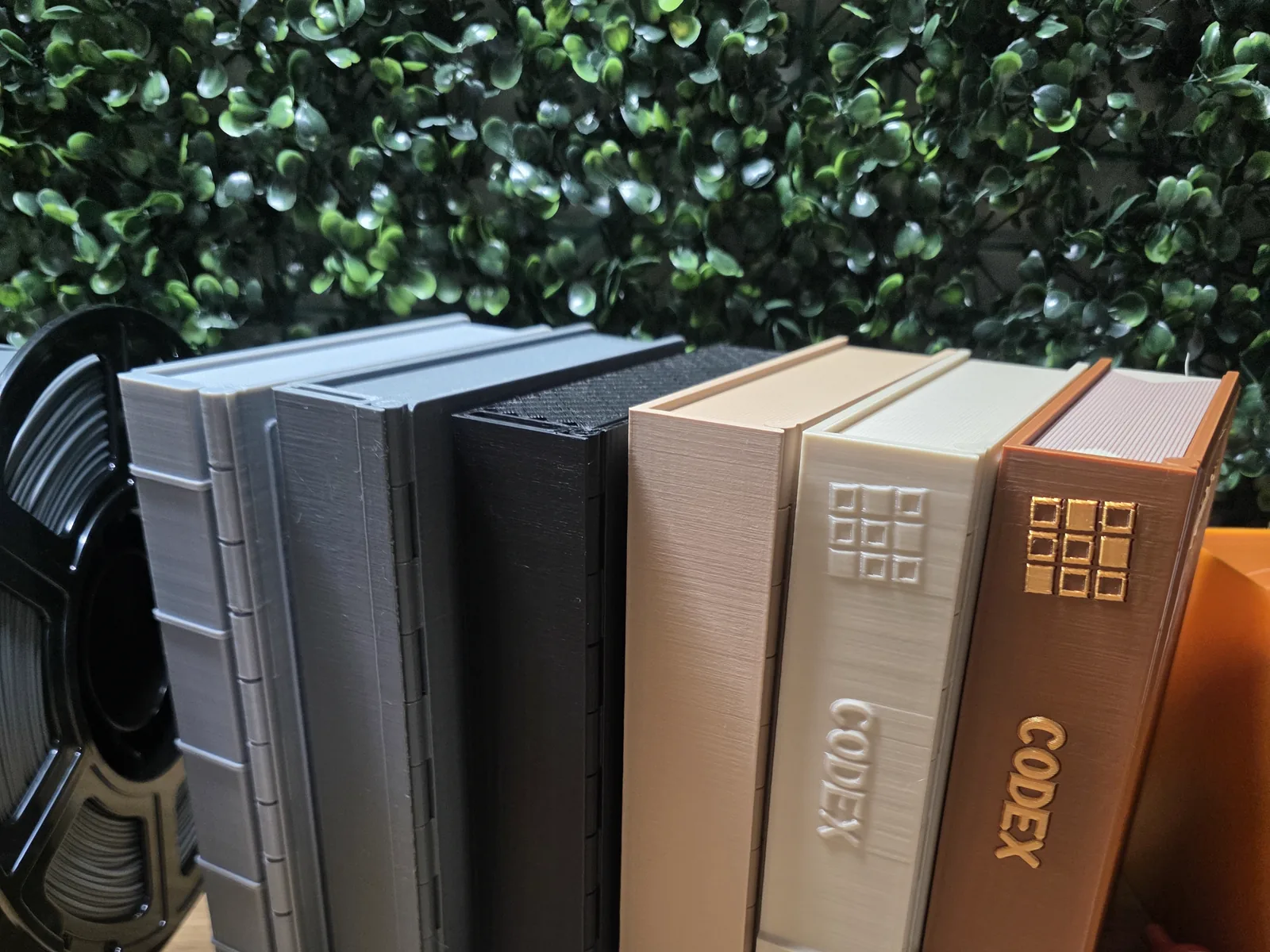 Six 3D-printed book prototypes in grey, black, cream and brown standing together on Jon’s workbench.